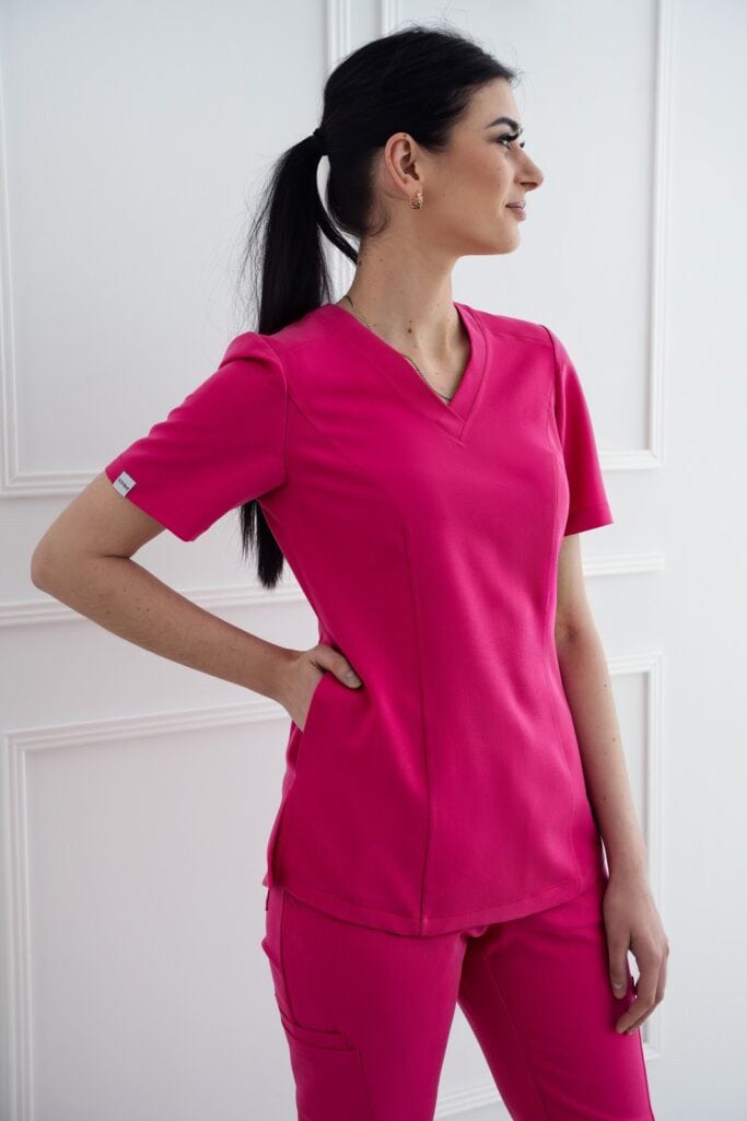 A woman in pink scrubs standing against a white wall